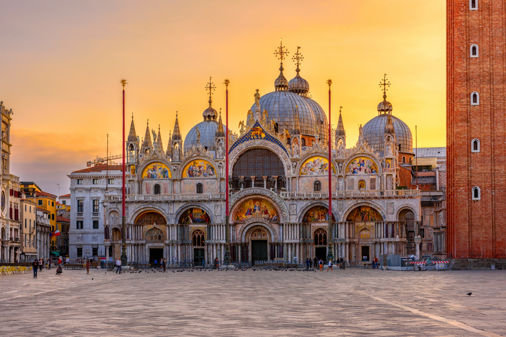 Golden sunrise over St. Mark's Basilica in St. Mark's Square with few people.