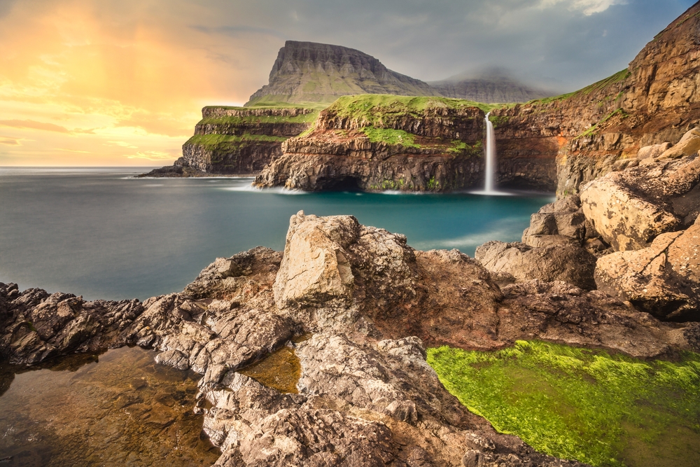 a waterfall falling into the ocean in the Faroe Islands, one of the best places to visit in europe in July