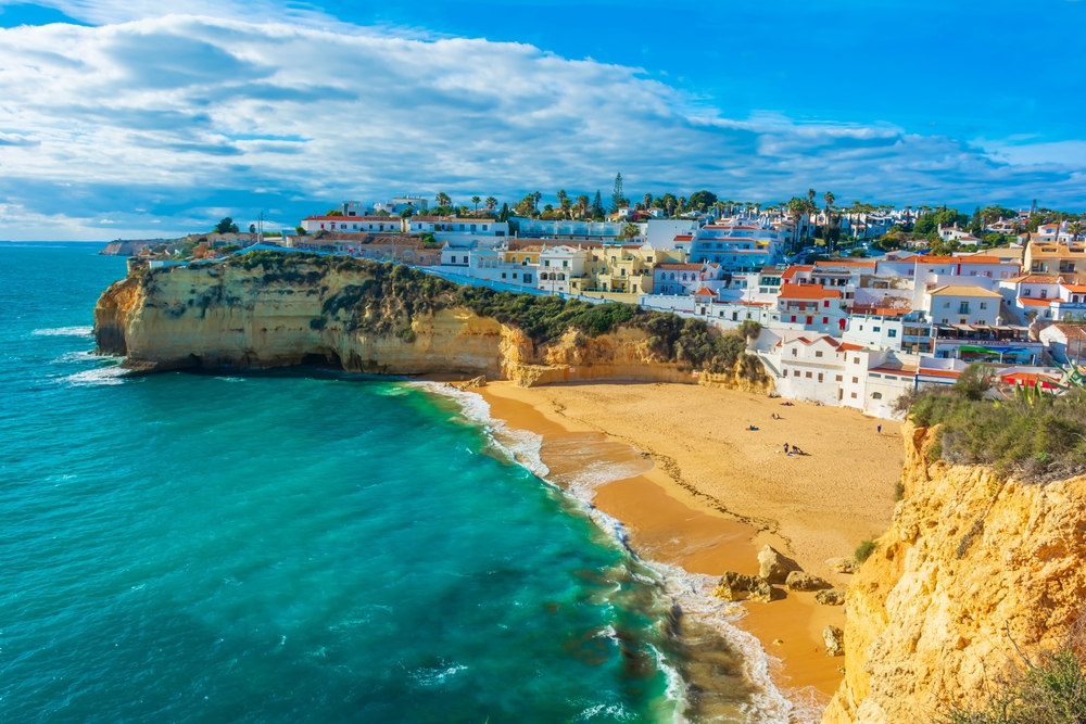 ocean to the left with dramatic cliffs and sandy beaches in the middle, behind that there are colorful buildings that are hotels, resorts, and restaurants 