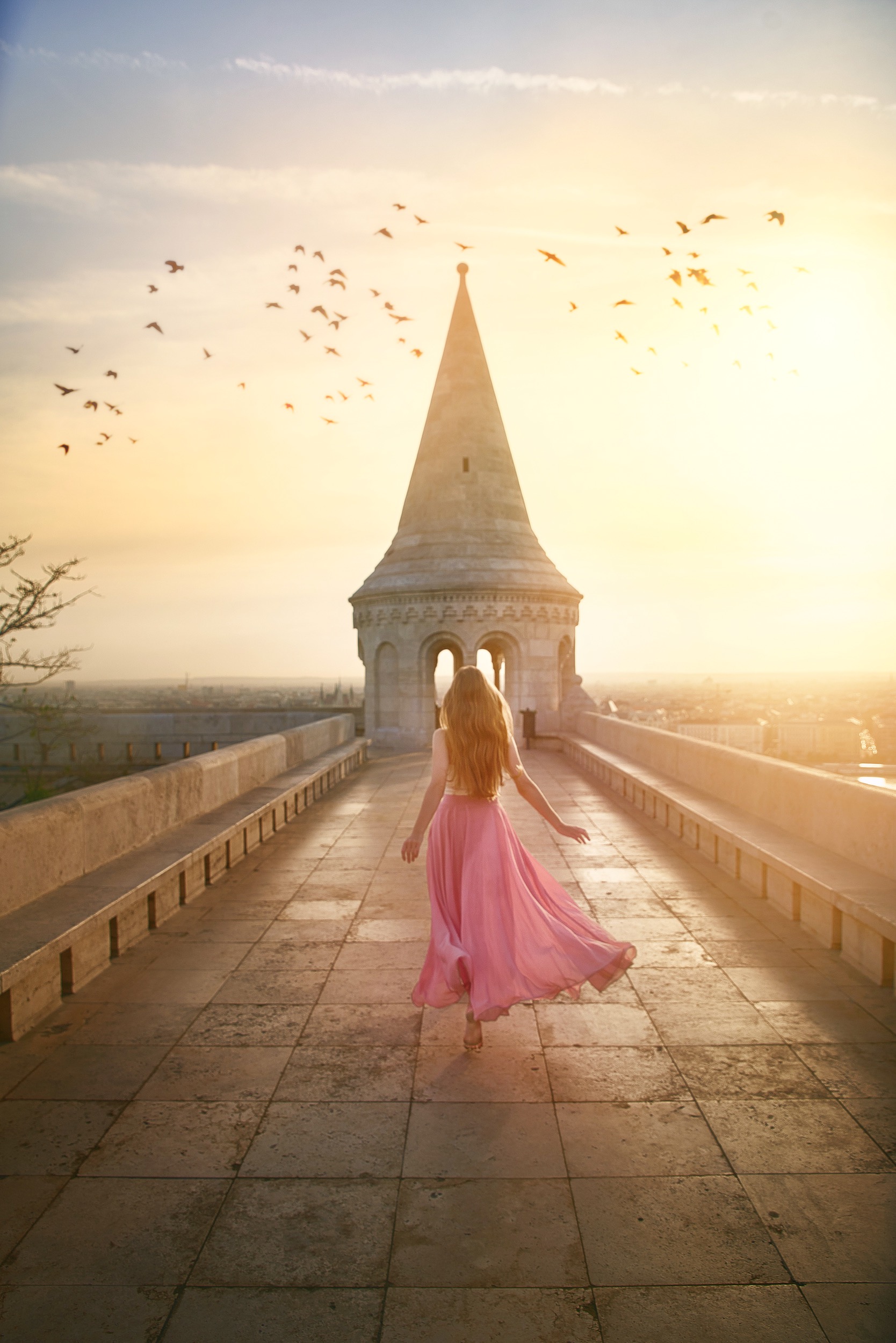 a woman in a long dress is running barefoot across a bridge to a steeple, there are many birds in the sky above her, one of the best places to visit in Europe in July 