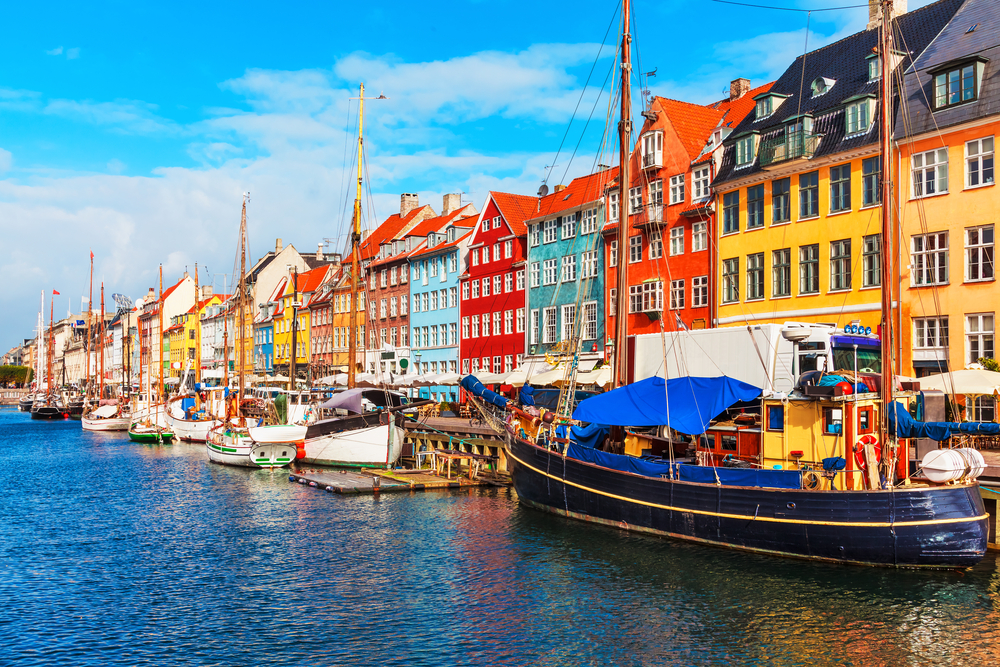 water is on the left and there is a row of boats docked on the waters edge, on the behind that there is a row of colorful houses lining the water, one of the best places to visit in Europe in July 