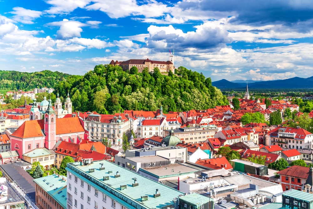 aerial photo of a castle on a hill with a city below it, there are mountains in the background and there are clouds in the sky 