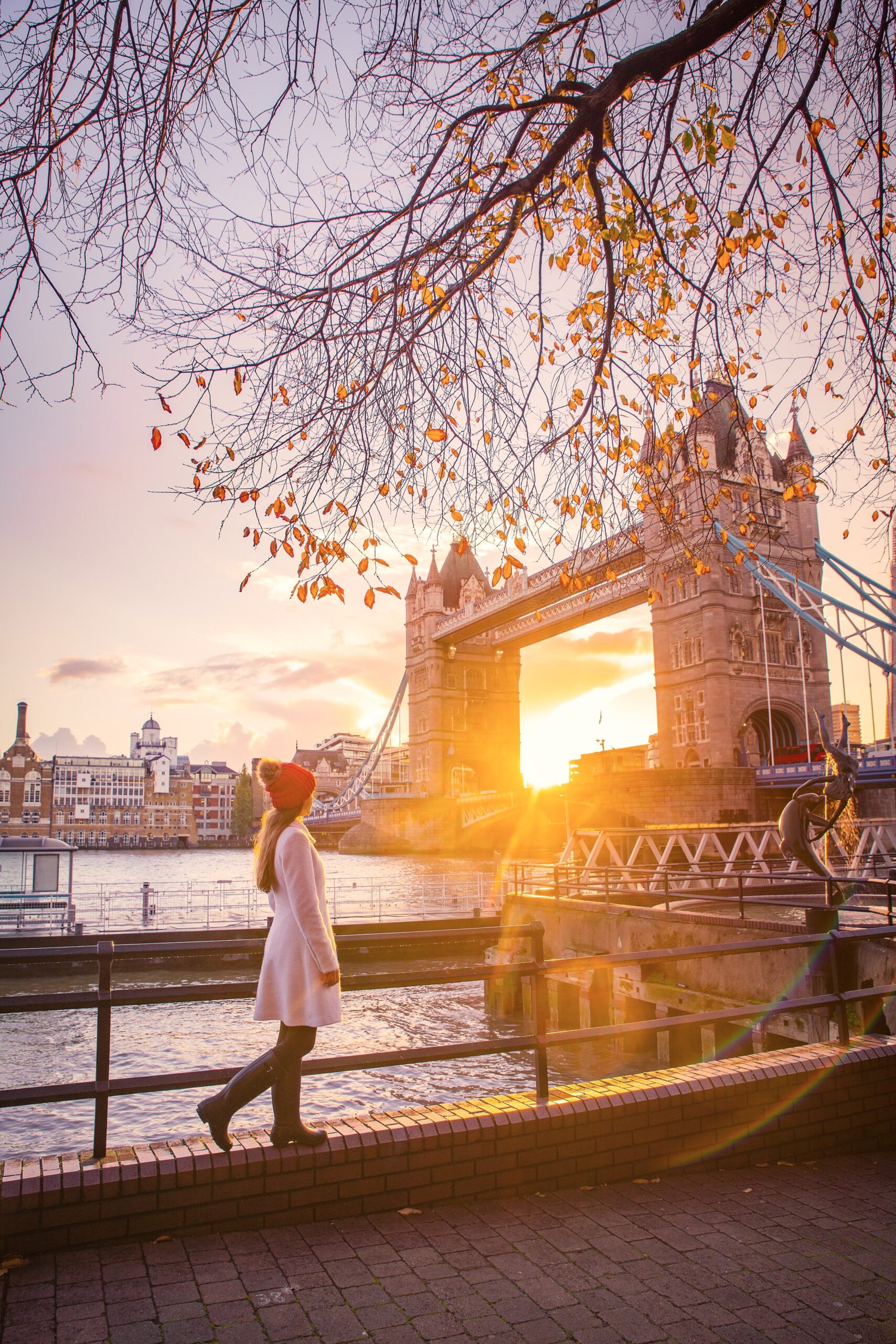 A girl in red hat and pink dress standing along the Thames overlooking the Tower Bridge at Sunset