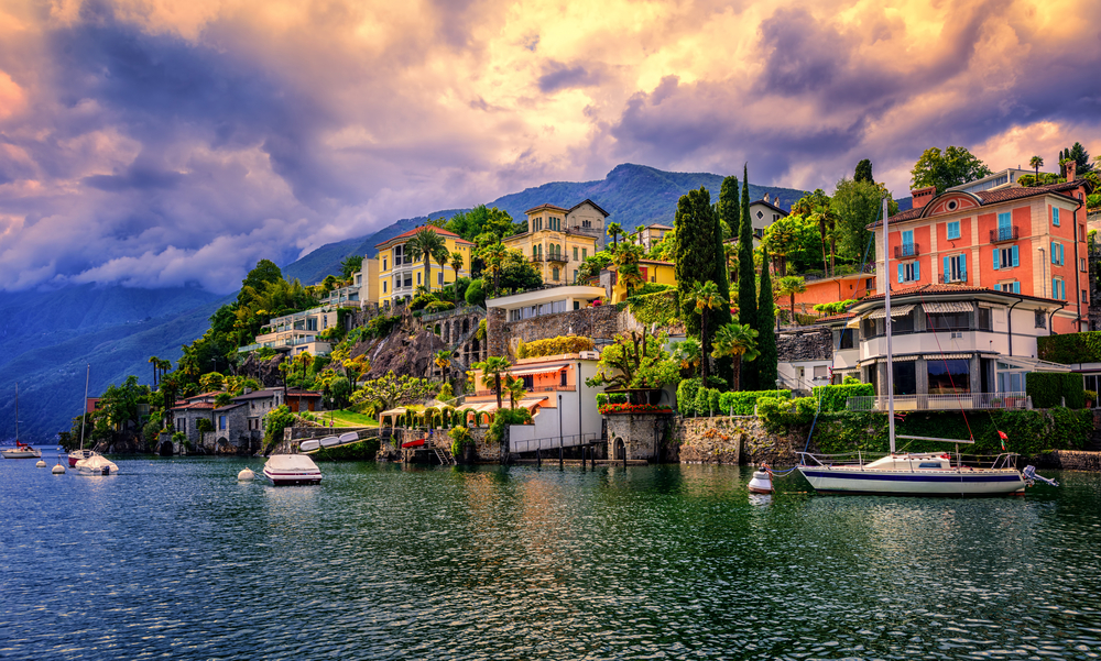 Dramatic sunset over Ascona, a popular resort town on Lago Maggiore. You can see buildings on the shore with boats.