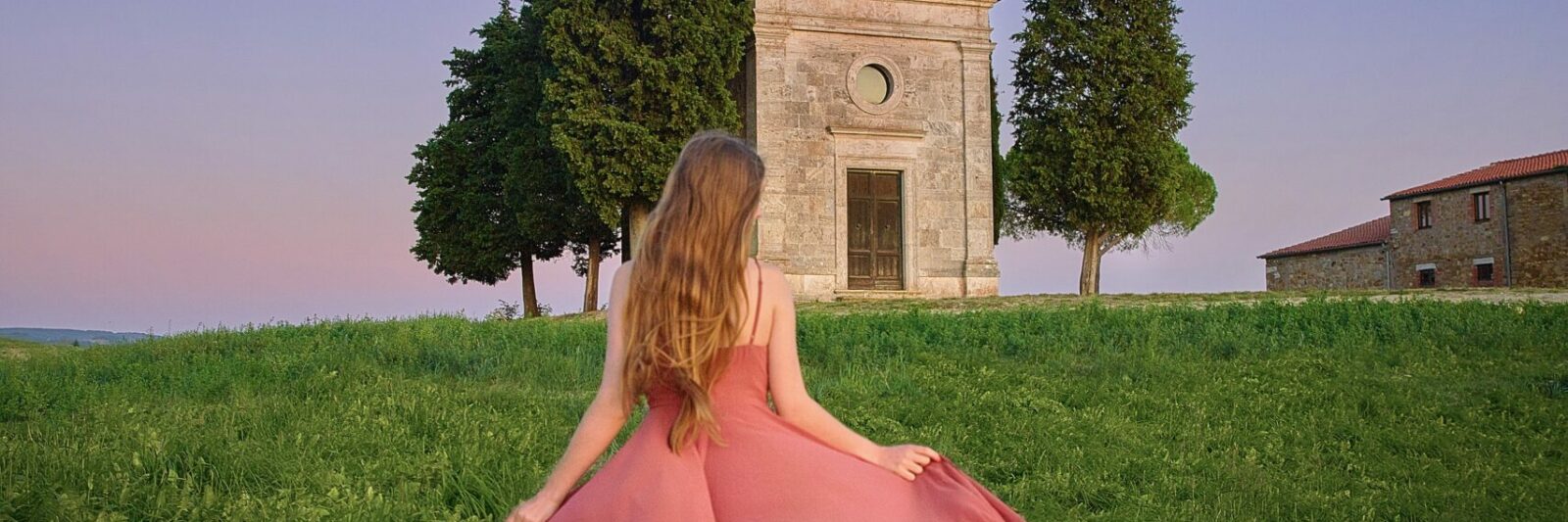 woman standing in Tuscany in a pink dress under the moonlight at a chapel