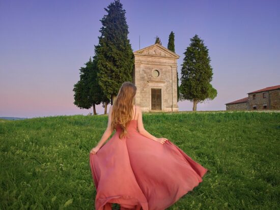 woman standing in Tuscany in a pink dress under the moonlight at a chapel