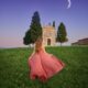 woman standing in Tuscany in a pink dress under the moonlight at a chapel