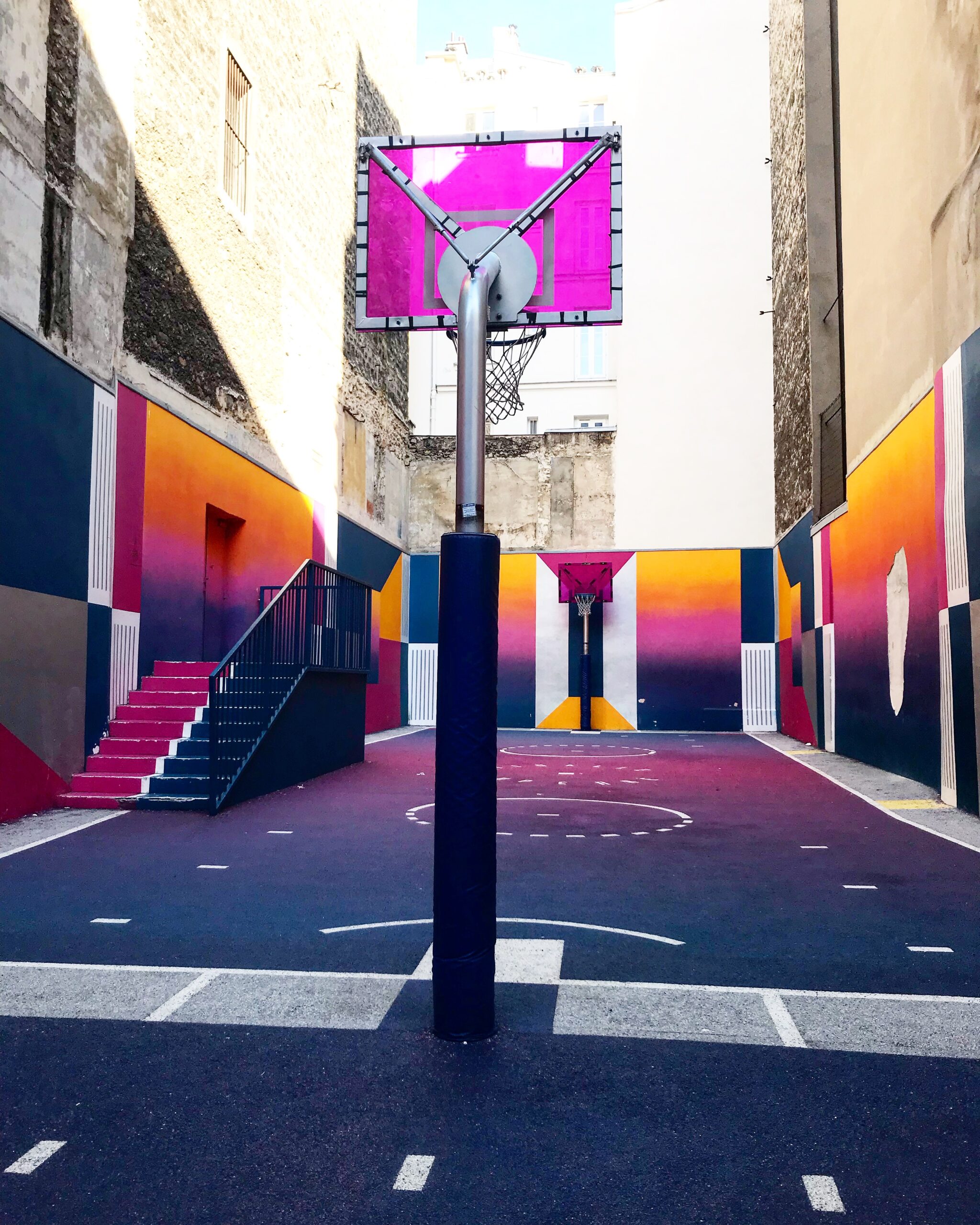 the Pigalle Basketball Court is purple, yellow and blue and a place you would want to visit. The court is empty. 