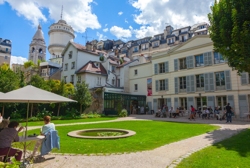 The Renoir Gardens at the Museum of Montmartre. There are people sat at tables and chairs. 