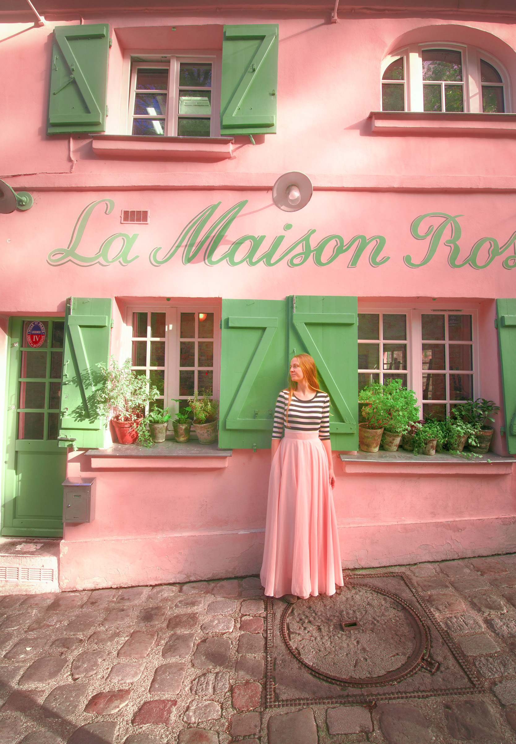 Girl in a pink skirt and striped top in front of the famus pink and green cafe one of the things to do in Montmartre