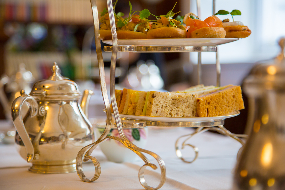A tiered tray of delicious high tea snacks served with a silver tea kettle