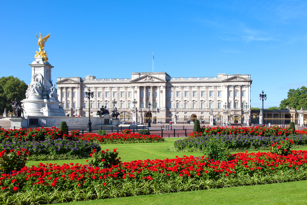  Buckingham Palace from across one for the gardens with flowers, and statues overlooking the gates of the palace