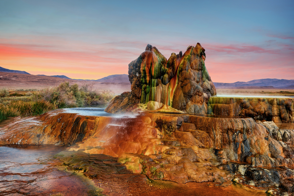 Sunset over the beautiful and colorful Fly Geyser with steaming water in a desert.