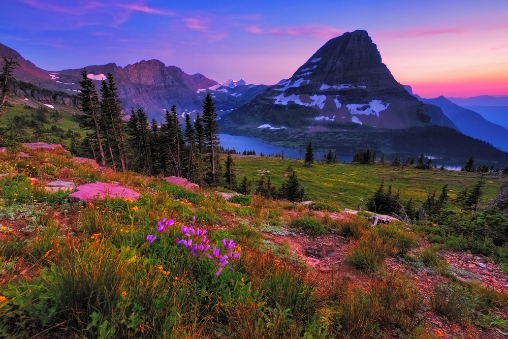 Vivid sunset over mountains, a lake, and wildflowers in Glacier National Park on a Montana road trip.