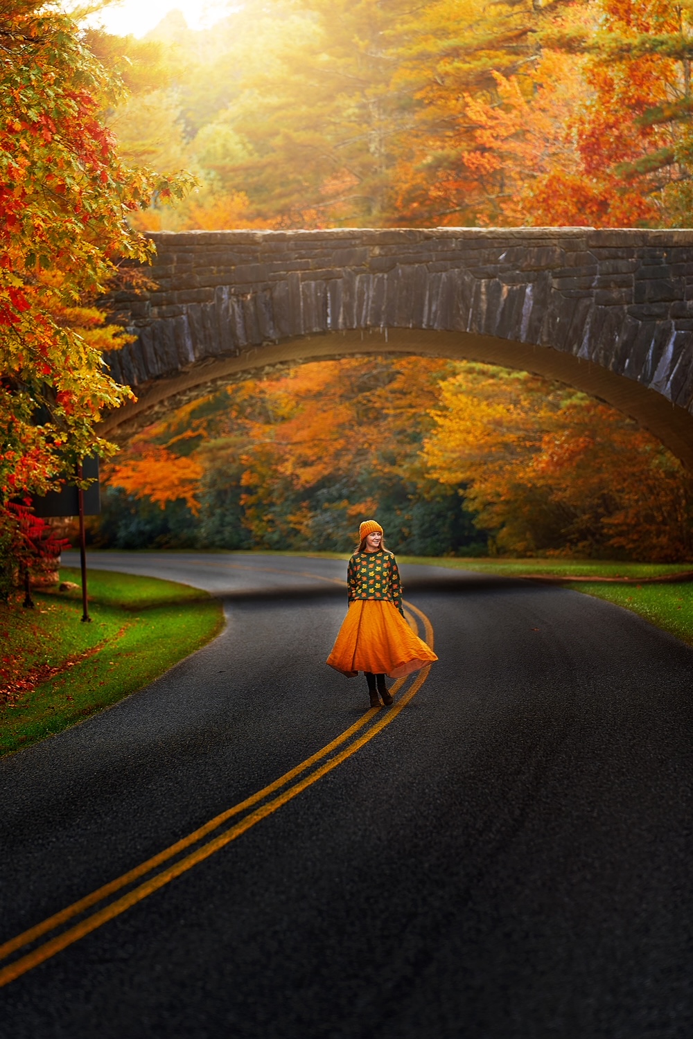 Woman in a flowing yellow skirt and leaf sweater walking on a highway under a bridge during fall on an East Coast road trip.