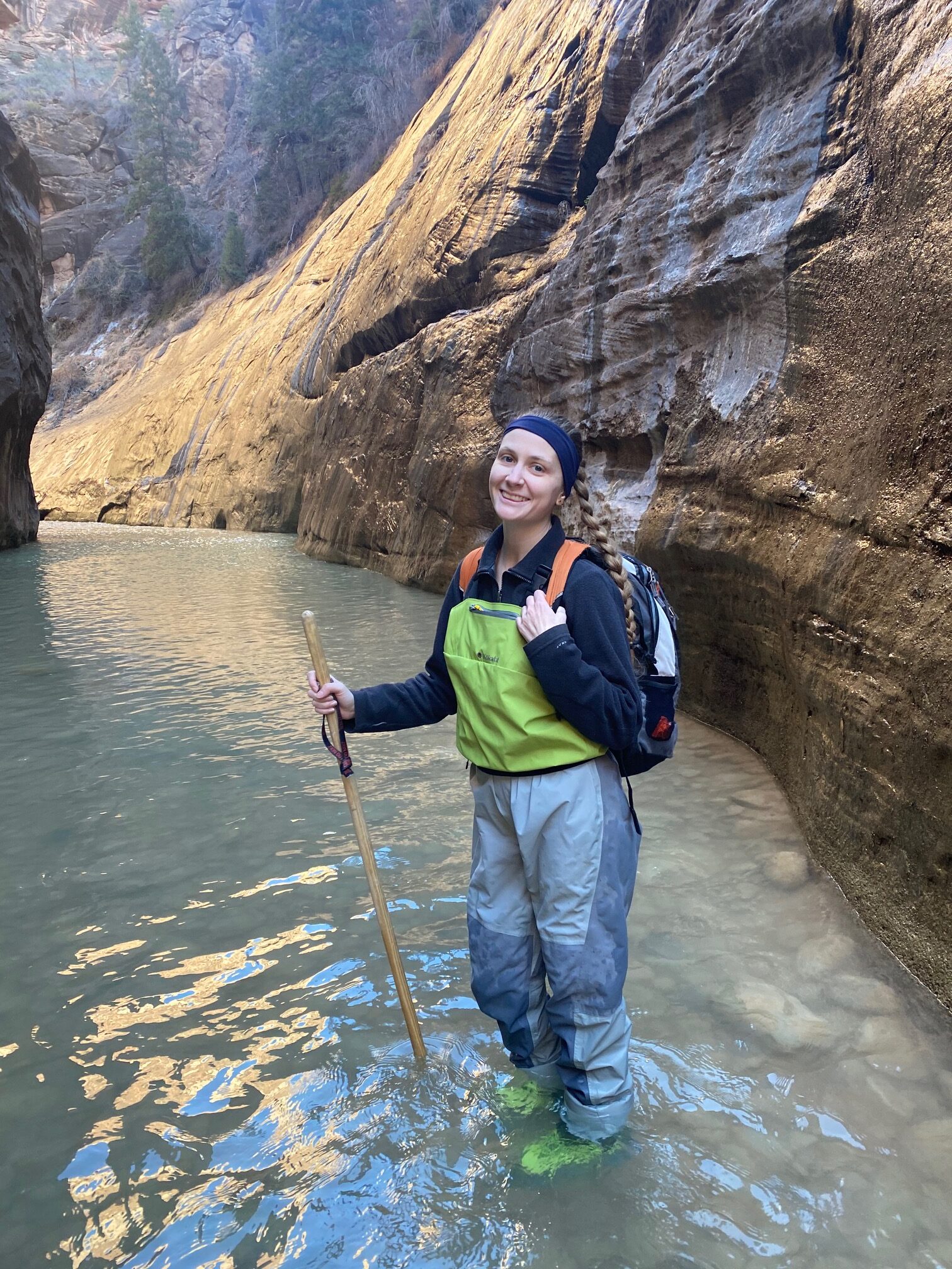 Woman in wading and hiking gear in the river of the narrows in Zion on a Utah road trip.