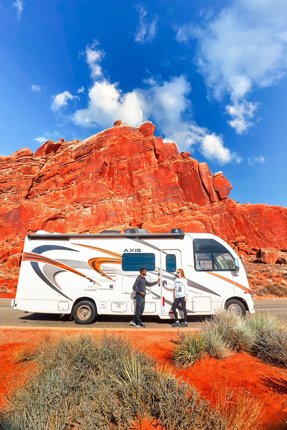 Couple standing on the side of an RV next to a red rock formation on a Utah road trip.