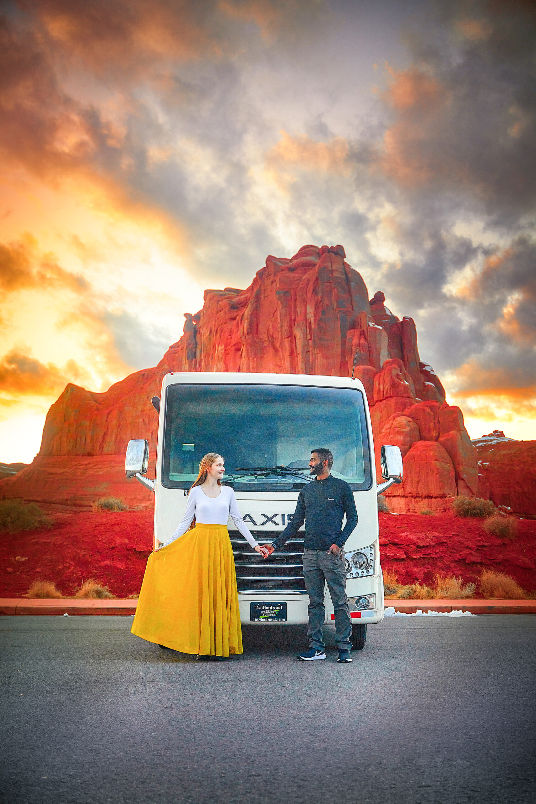 Couple holding hand in front of an RV with a rugged red rock in the background at sunset on a Utah road trip.