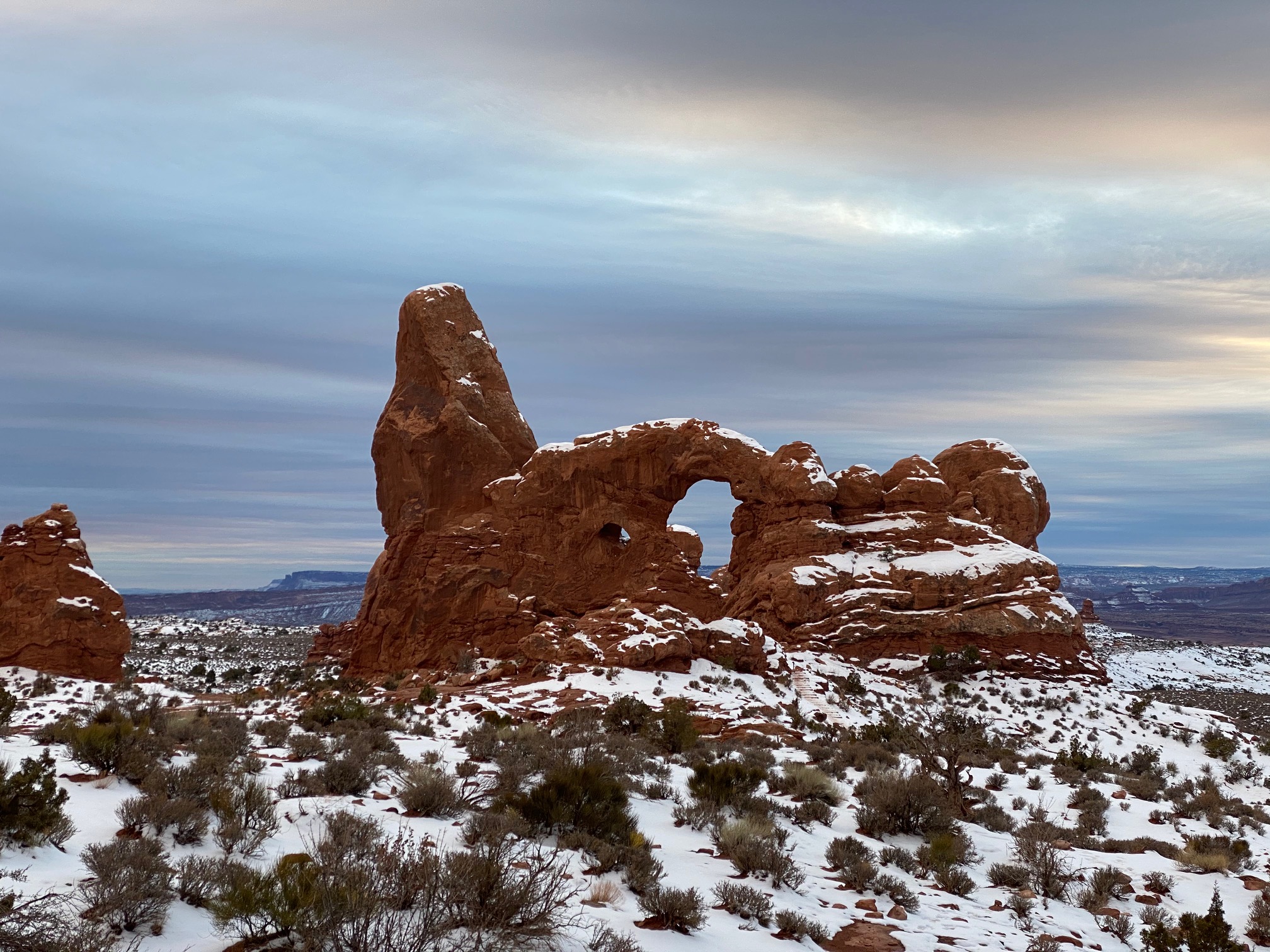 Overcast day at Arches National Park with some snow on the ground and one big rock formation with an arch.