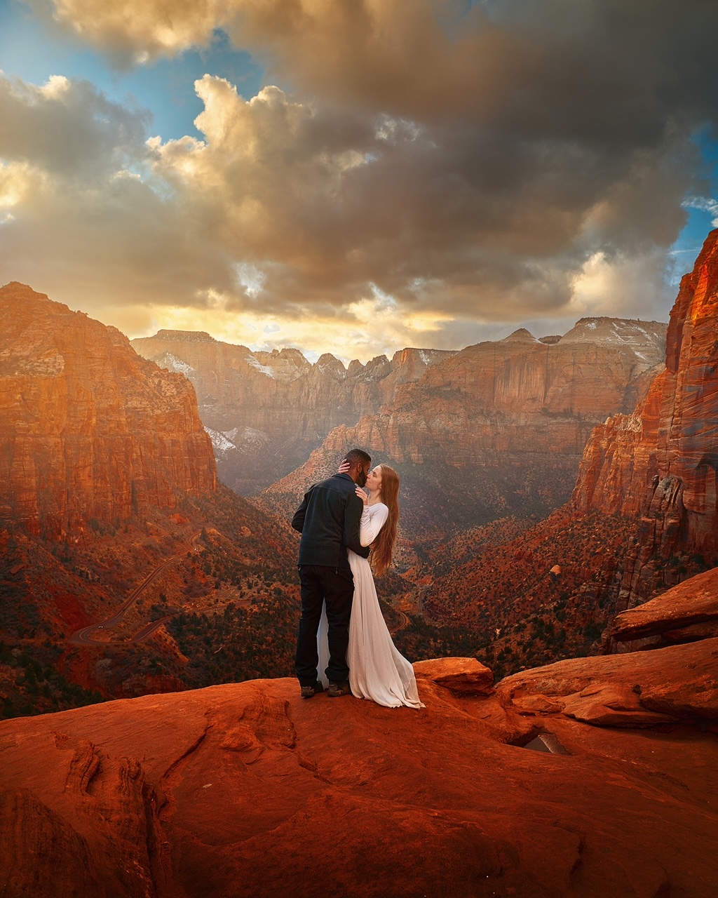 Couple kissing on the edge of a panoramic vista in Zion National Park at sunset on a Utah road trip.