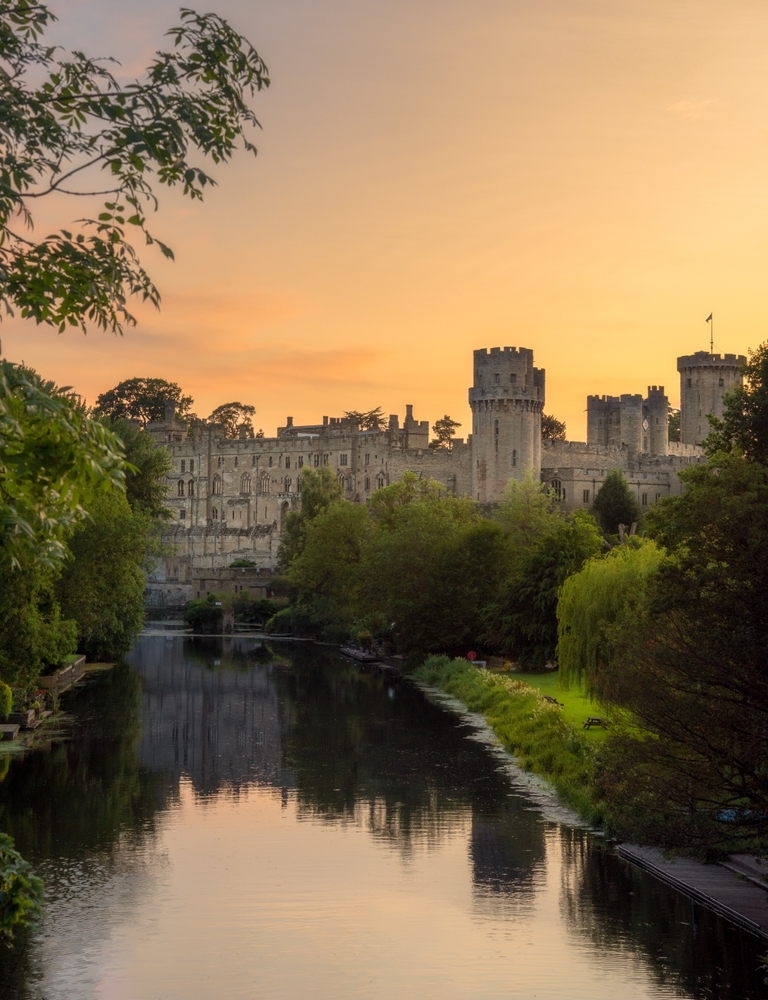 Warwick castle taken from across the moat showing the side of the castle with trees around me. 