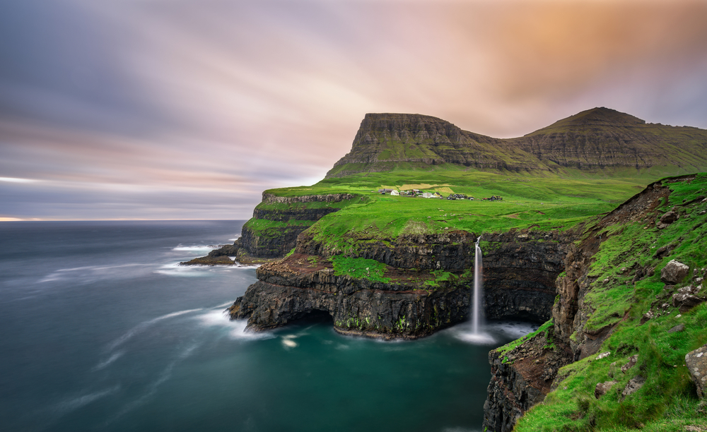 ocean to the left, an island to the right that has a waterfall falling into the ocean, Faroe Islands 