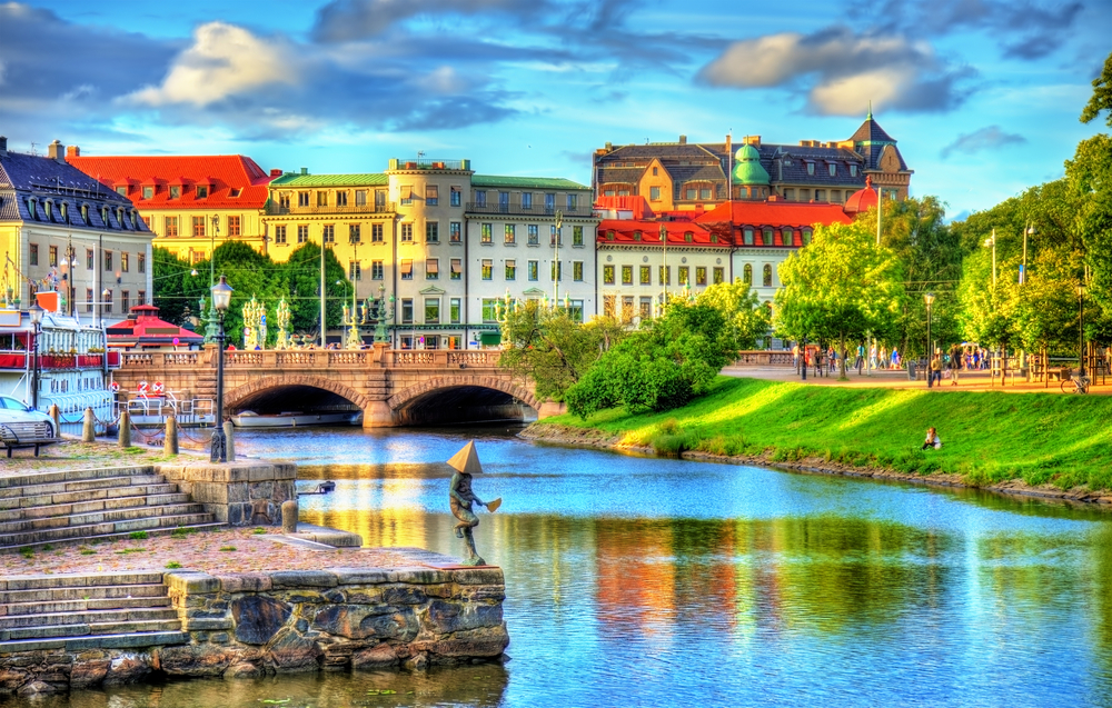 a statue next to the river, a bridge crosses the water, buildings are in the background of Gothenburg, one of the best things to do in Europe in June 