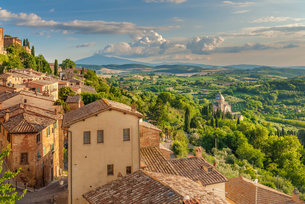 tuscan houses to the left, hills and green fields to the right of the photo on a cloudy day in Italy 