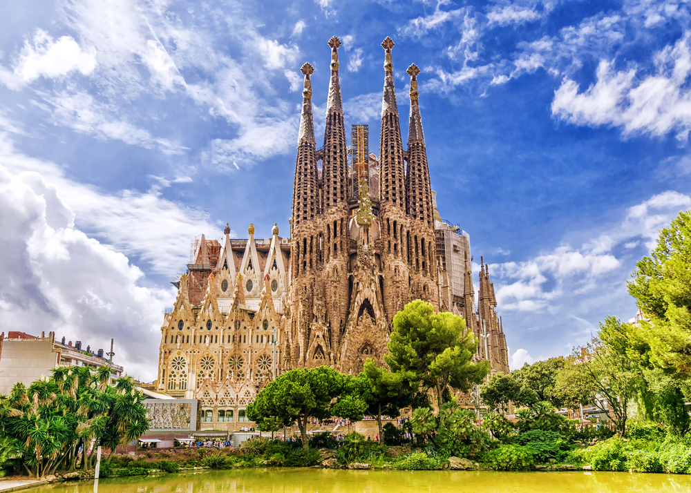 a tall historic church stands in front of trees and a body of water in barcelona, one of the best places to visit in europe in september 