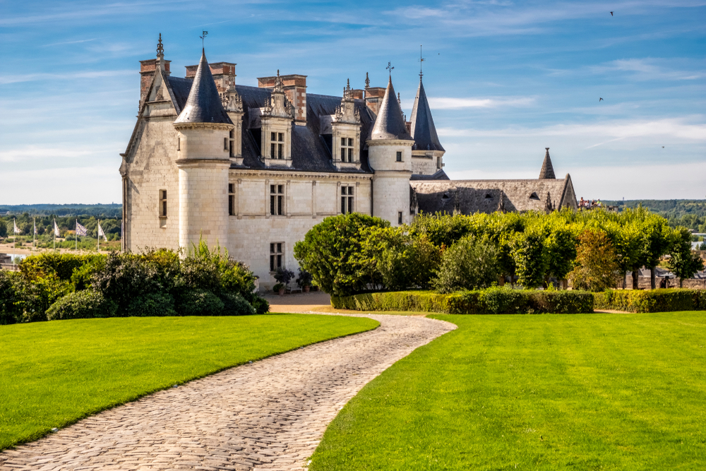 a castle in france with pointy spires on top, a long cobblestone pathway leads to the castle 