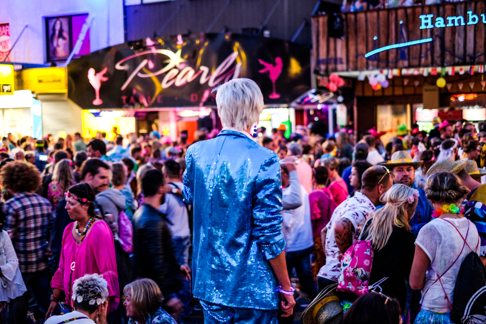 a festival in europe, the streets are crowded and a person in a sequined suit is standing in the middle with back to the camera 