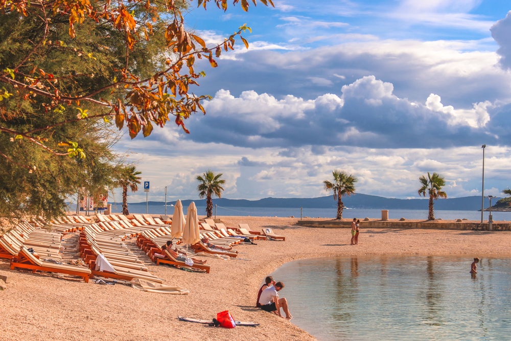 a curved beach in croatia, mountains in the background, beach chairs are lined up on the beach 
