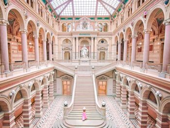 woman standing in a pink skirt on stairs in vienna austria. the whole scene is indoors with a glass roof