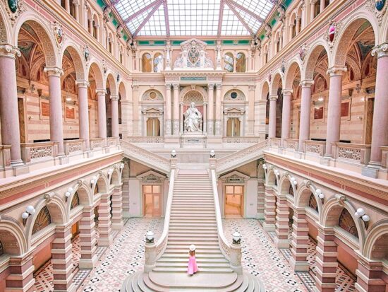 woman standing in a pink skirt on stairs in vienna austria. the whole scene is indoors with a glass roof