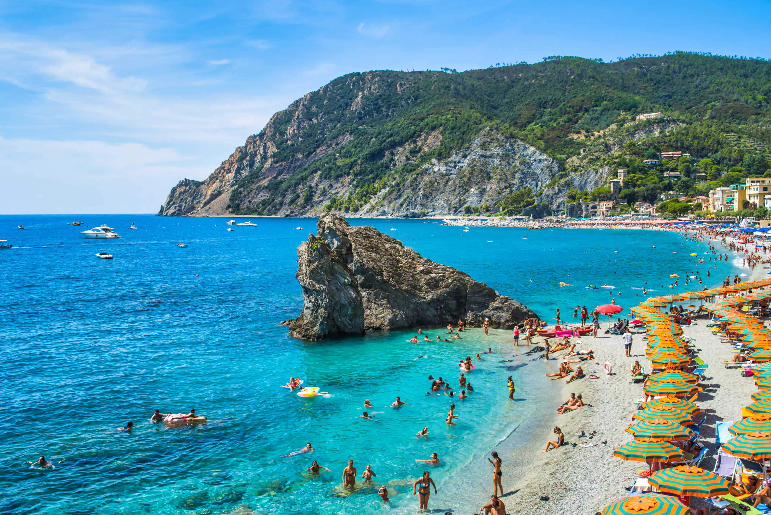 colorful green and orange umbrellas dot the sand and lots of people play in the ocean at Fegina beach