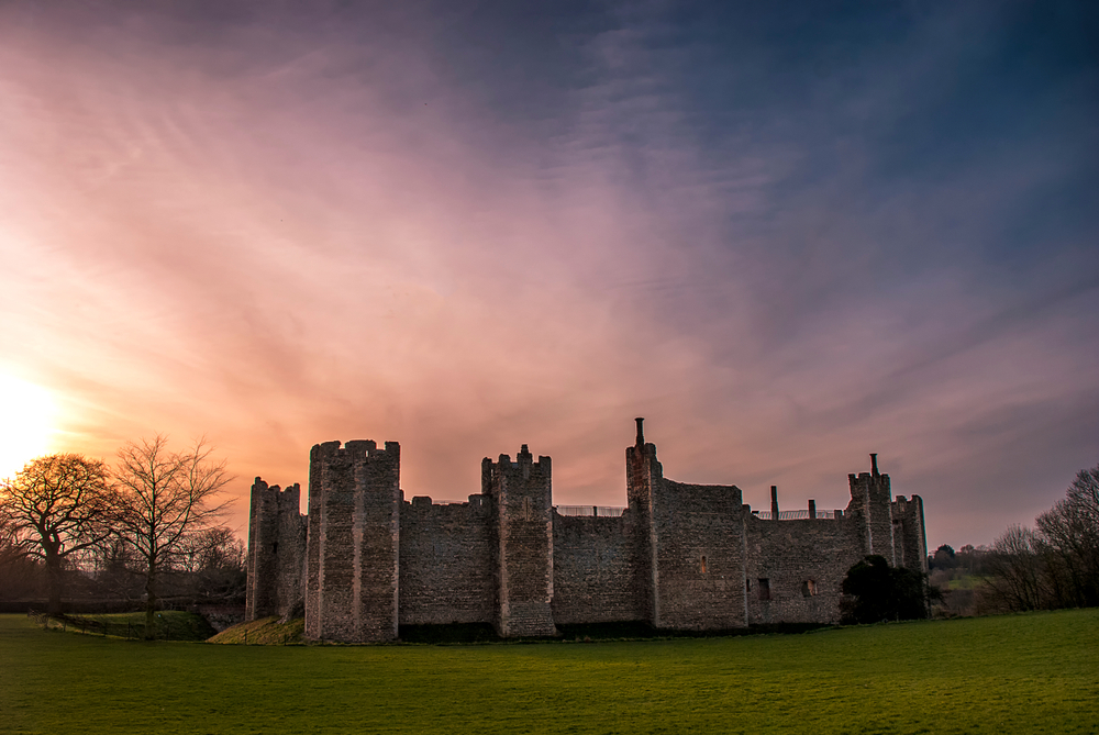Sunset over Framlingham Castle. The castle is in a field and you can see trees behind it. 