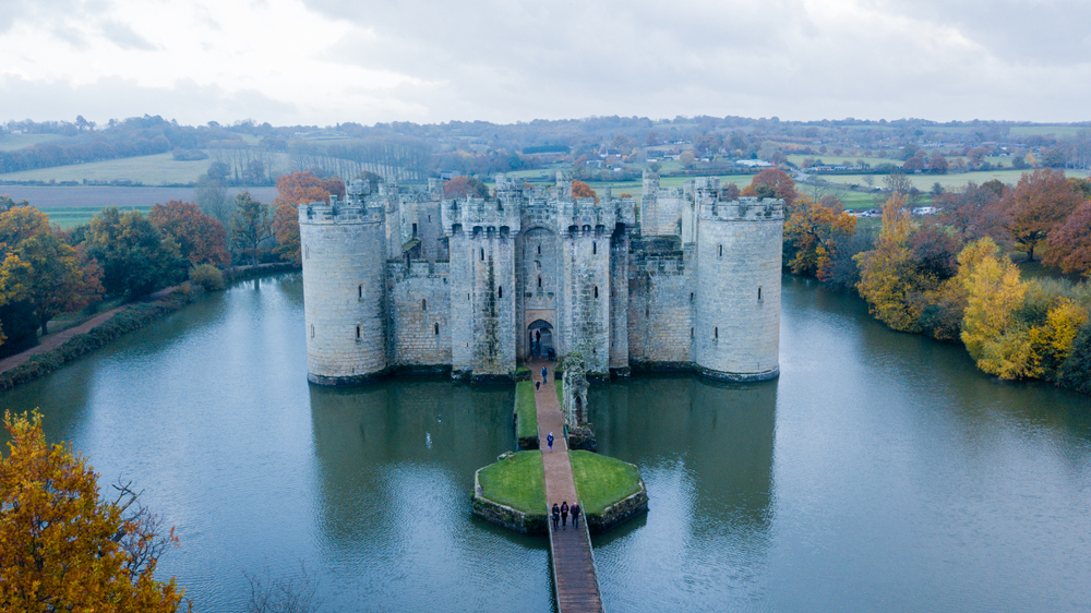 Bodiam Castle from the Sky. You can see the castle surrounded by water and fall foliage, It is one of the castles near London. 