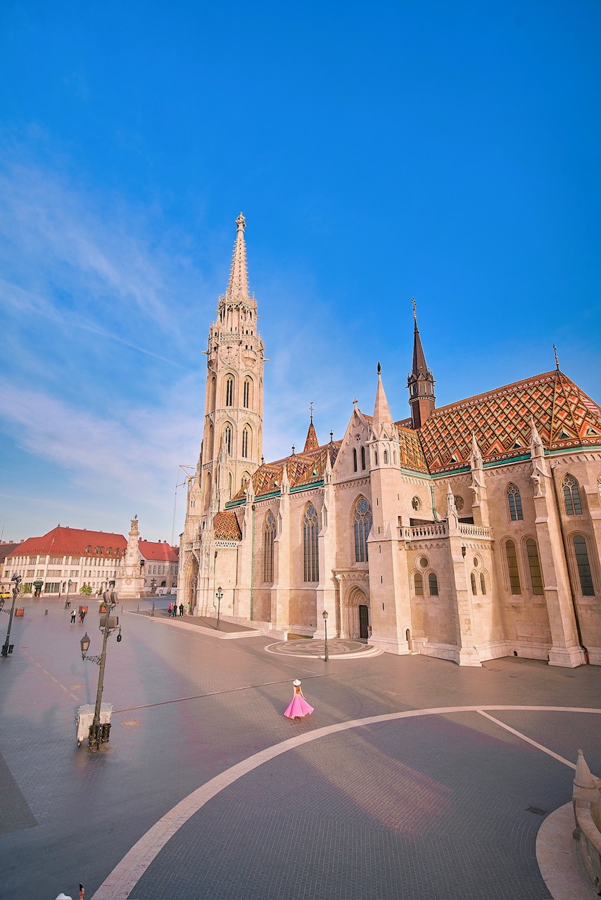 woman long dress standing in front of tall church on a bright day in Budapest Hungary 