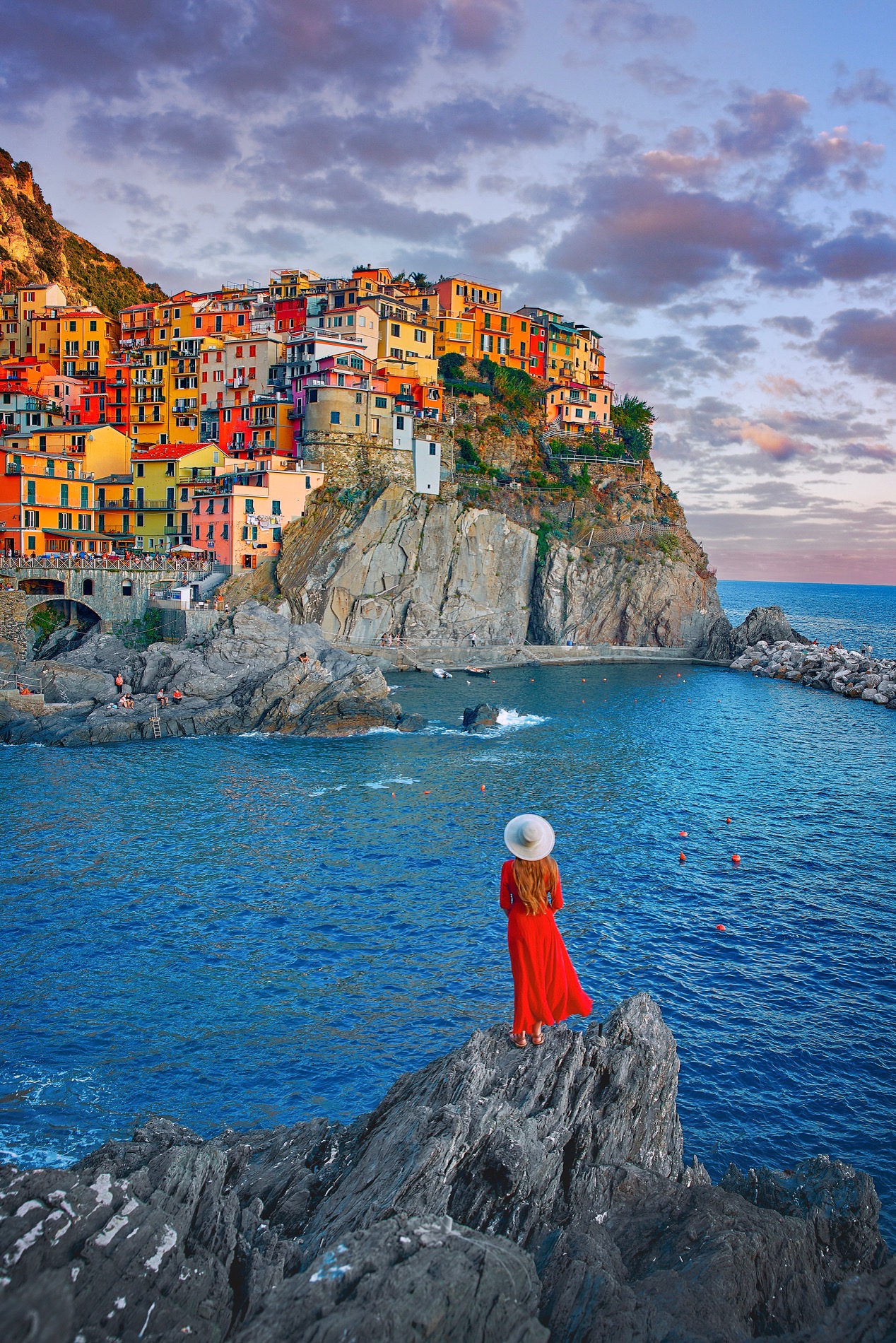 best places to visit in Europe in October, cinque Terre in the evening, a woman is standing in the middle of the photo on a rock, she is wearing a long dress and a hat 