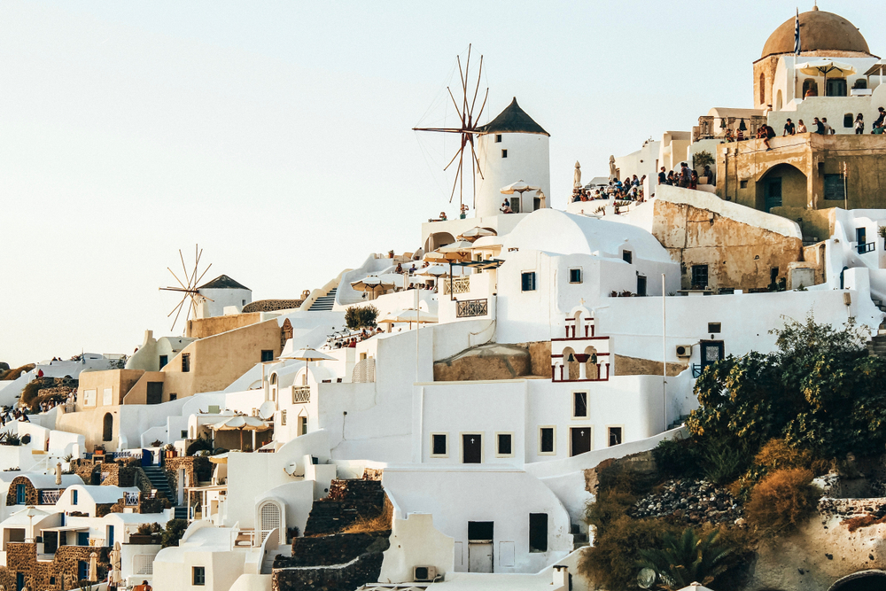 a hillside city in the greek isles with people standing on stairways between buildings