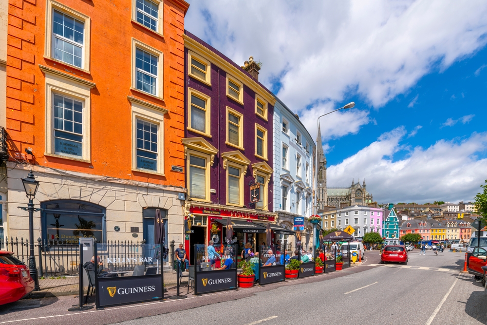 Saint Colman's Cathedral can be seen above the pubs and shops along the main seaside street in Cobh, Ireland