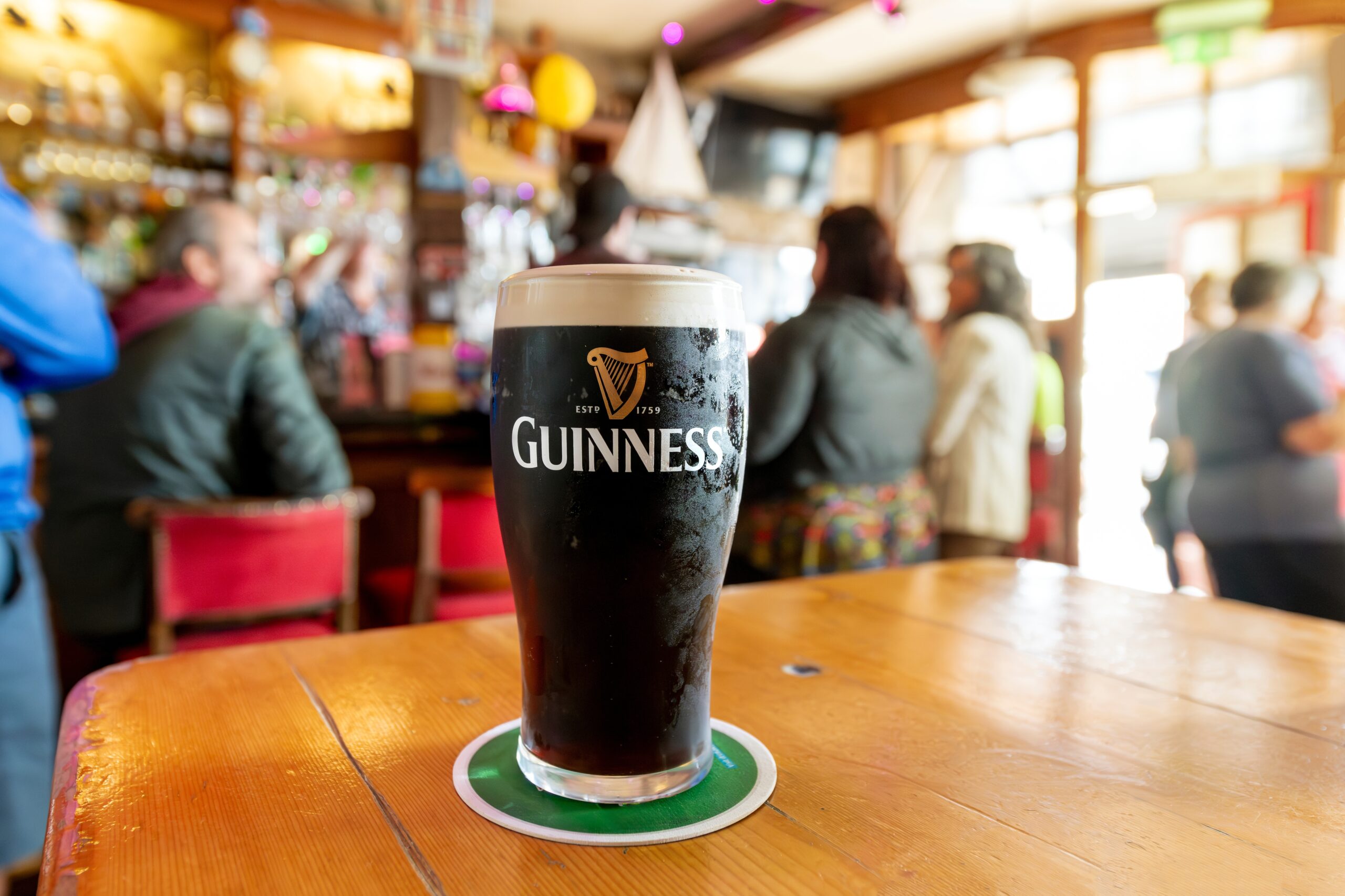 view of a full pint of Guinness Irish dry stout Beer in a colorful busy pub in the city of Cobh, Ireland