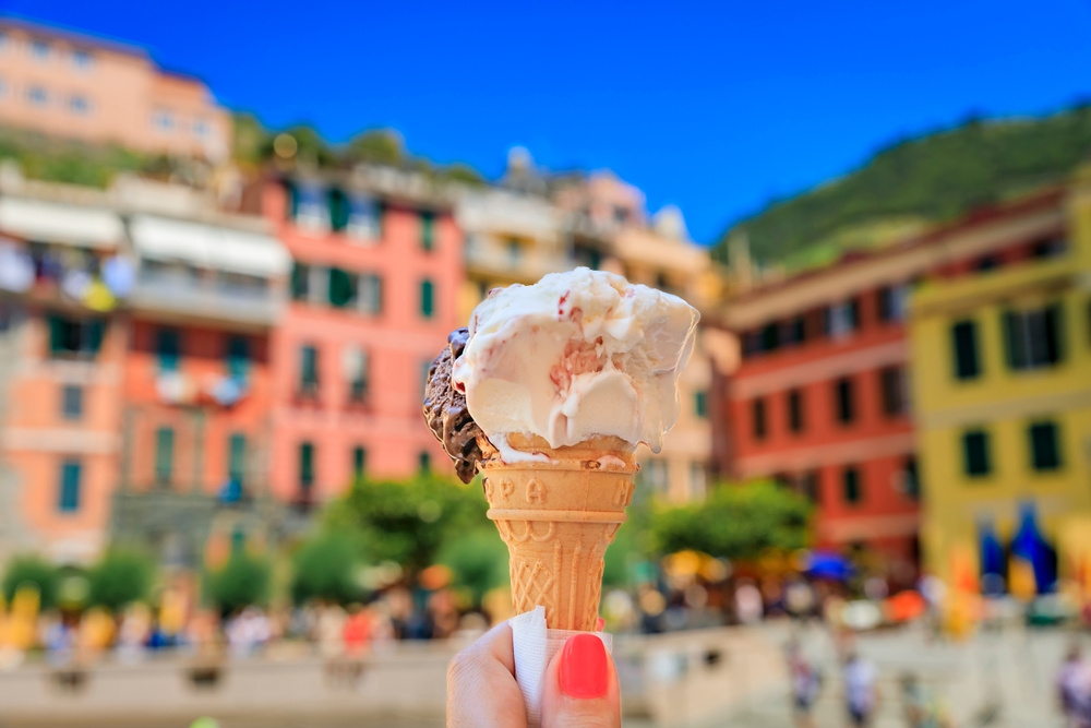 Hand holding an artisanal gelato, a view of traditional colorful houses in old town of Vernazza in Cinque Terre on the Mediterranean Sea, Italy