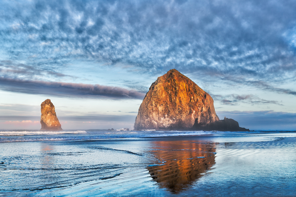 Sunset over Cannon Beach with a big sea stack and blue clouds during an Oregon road trip.