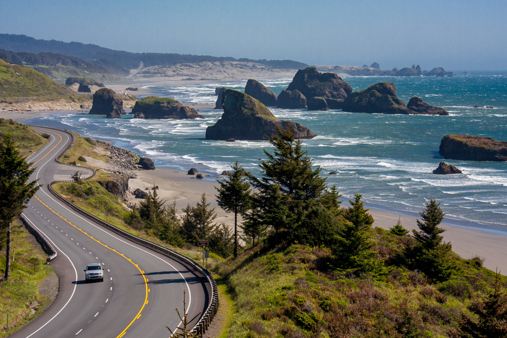 Winding highway along the pretty Oregon coast and Cannon Beach with big rock formations in the water on an Oregon road trip.