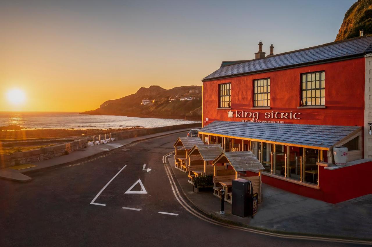 Orange sunset over the ocean next to the red-painted King Sitric with cute outdoor seating.