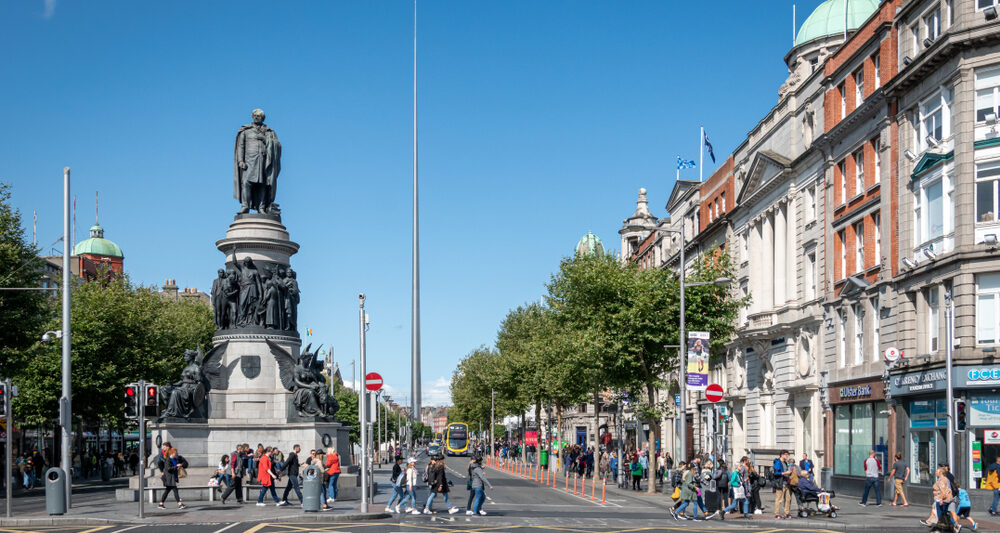 People walking around O'Connell Street next to a big statue of multiple figures.