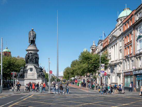 People walking around O'Connell Street next to a big statue of multiple figures.