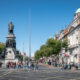 People walking around O'Connell Street next to a big statue of multiple figures.