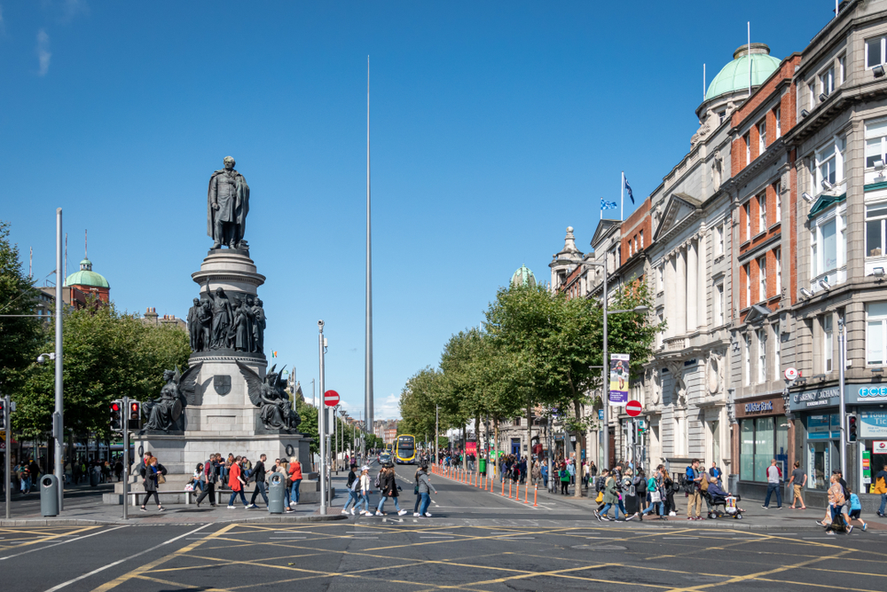 People walking around O'Connell Street next to a big statue of multiple figures.